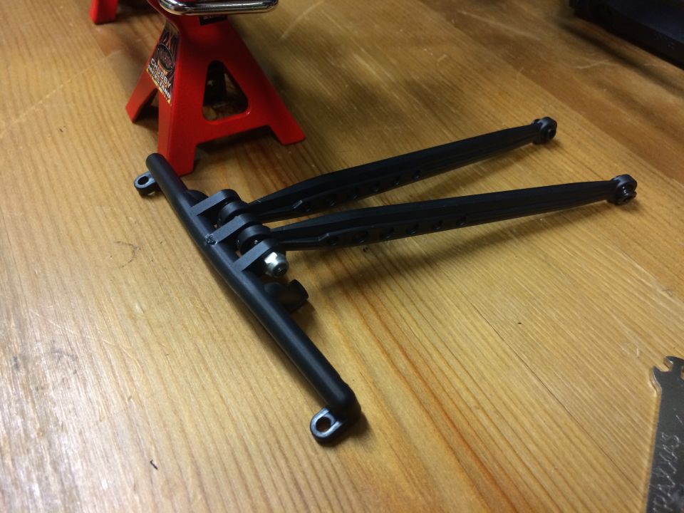 Black plastic suspension arms on a wooden surface with a red jack stand