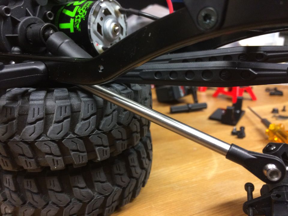 Close-up of RC car suspension and tires, showing a metal rod linkage.