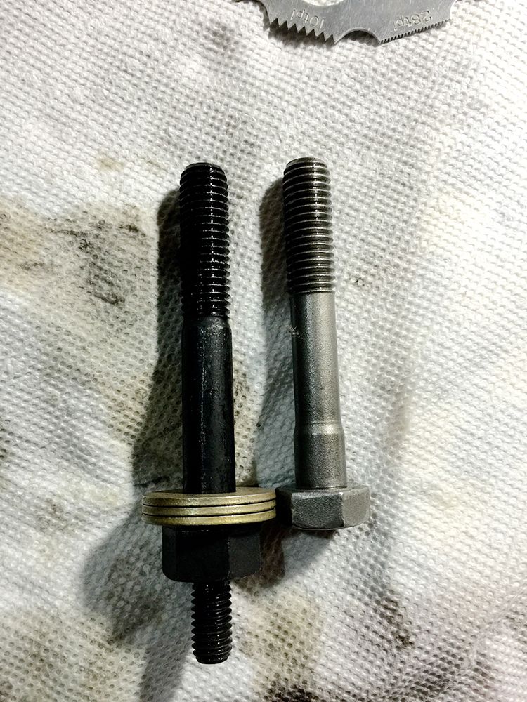 Two bolts on a white cloth. One is black with washers and a nut, the other is silver.