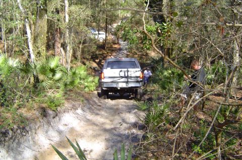 1993 Ford Bronco - A 1993 Ford Bronco navigates a challenging dirt path through a forest, with another vehicle ahead.