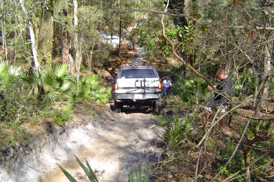 Rear view of white lifted Ford Bronco on a sandy wooded off-road trail
