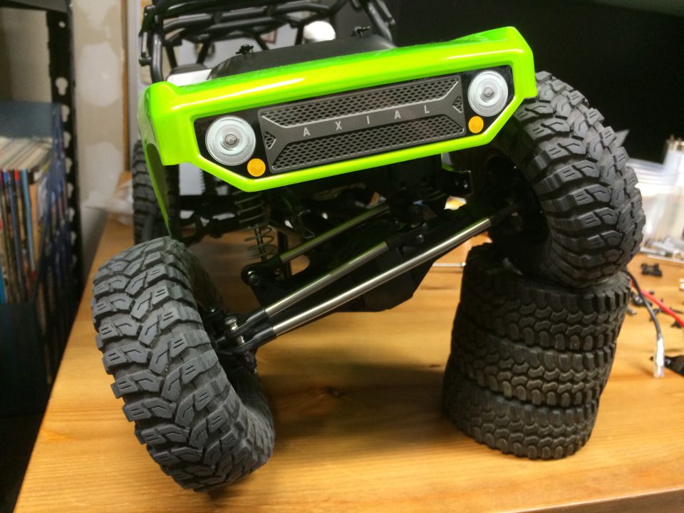 Green RC rock crawler front end with Axial logo and knobby tires stacked.