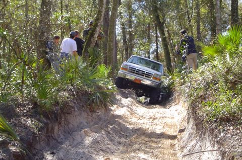 1993 Ford Bronco - A Ford F-Series truck navigates a challenging off-road trail surrounded by trees and onlookers.