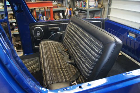 1979 Ford Bronco - The interior of a blue Ford Bronco shows a rear bench seat with striped fabric and black vinyl bolsters, equipped with seatbelts. The view…