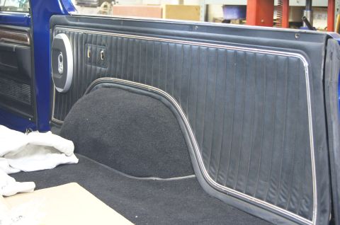 1979 Ford Bronco - The interior of a classic blue Ford Bronco shows the black upholstered side panel with chrome trim and a carpeted wheel well. A white cloth…