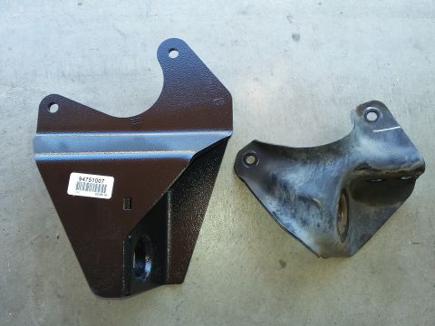 1996 Ford Bronco - A new black metal bracket with a part number sticker sits next to an older, weathered black metal bracket. Both appear to be suspension or…