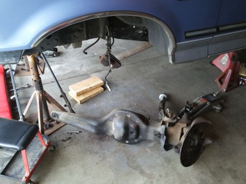 1996 Ford Bronco - A disassembled rear axle assembly is laid out on the concrete floor beneath a blue Ford Bronco. The vehicle is supported by jack stands and…