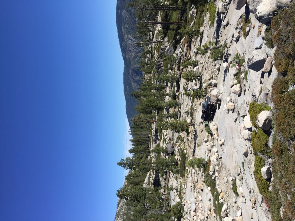 Photo of an off-road vehicle on granite terrain among pine trees