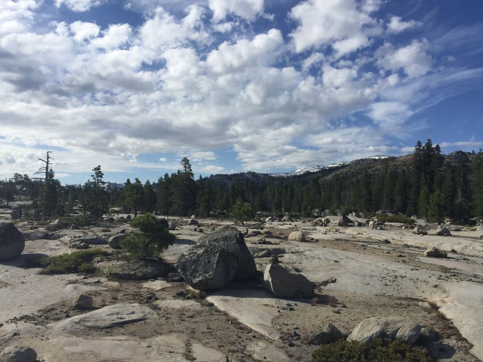 Photo of a granite landscape with boulders, pines and clouds
