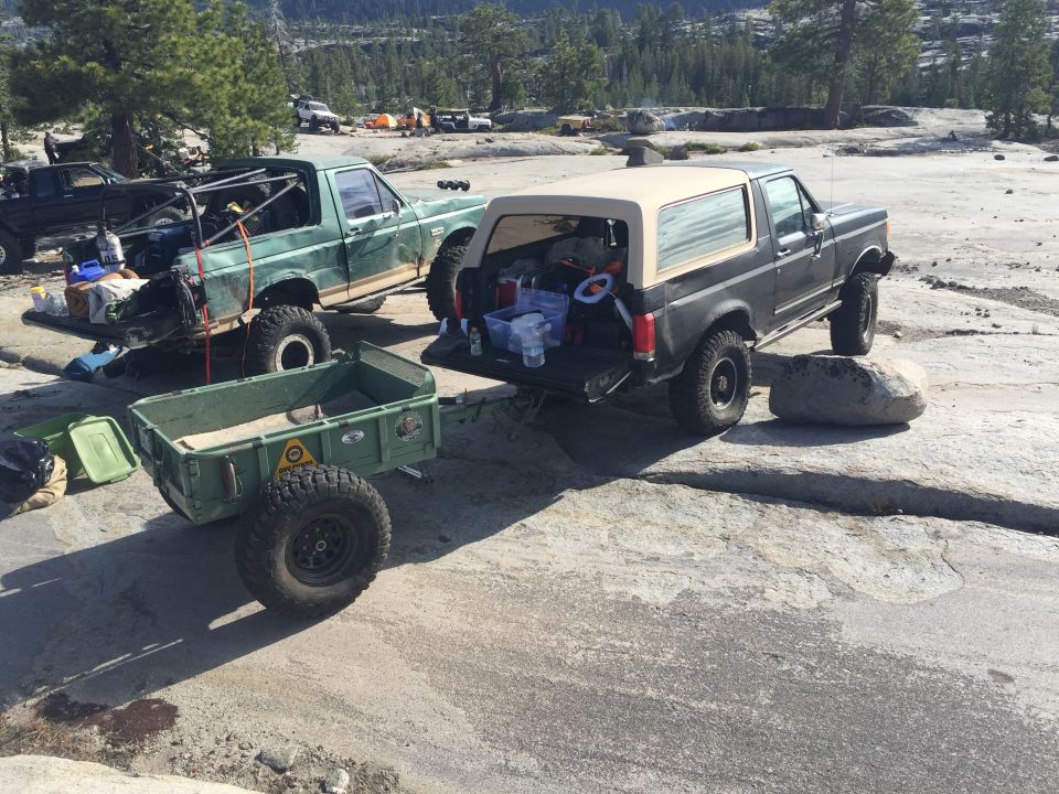 Photo of a Bronco and trucks with a trailer on granite terrain