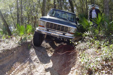 1993 Ford Bronco - A dark blue 1978 Ford Bronco navigates a steep dirt incline in a wooded area.