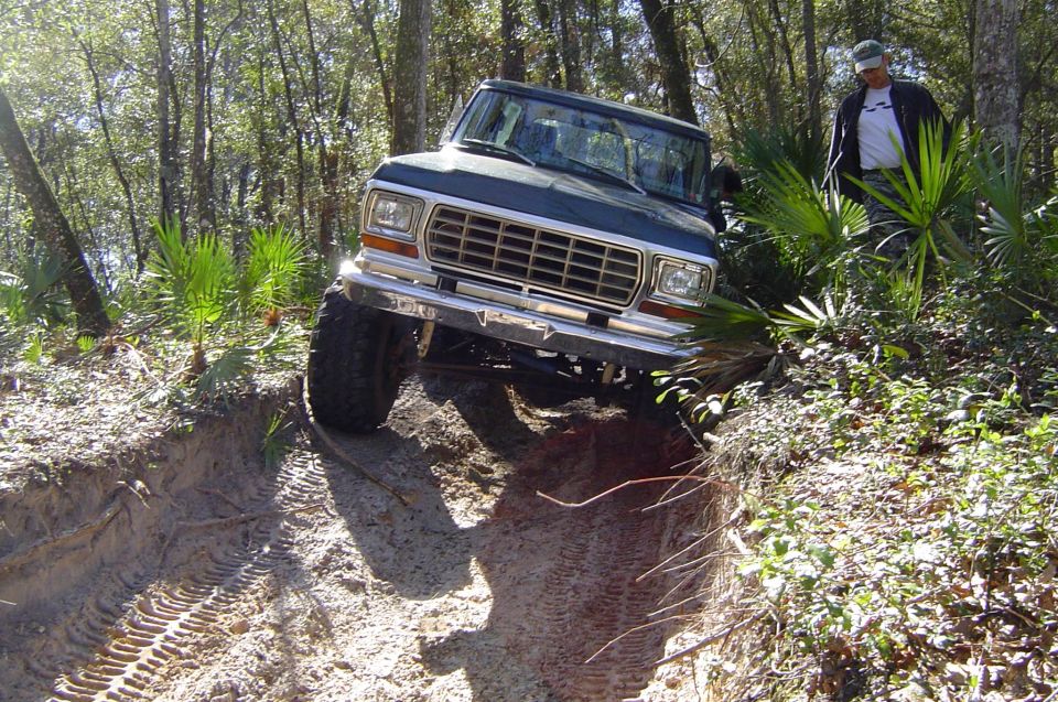 Dark green late-70s Ford 4x4 dropping into a sandy trail washout with a spotter standing nearby