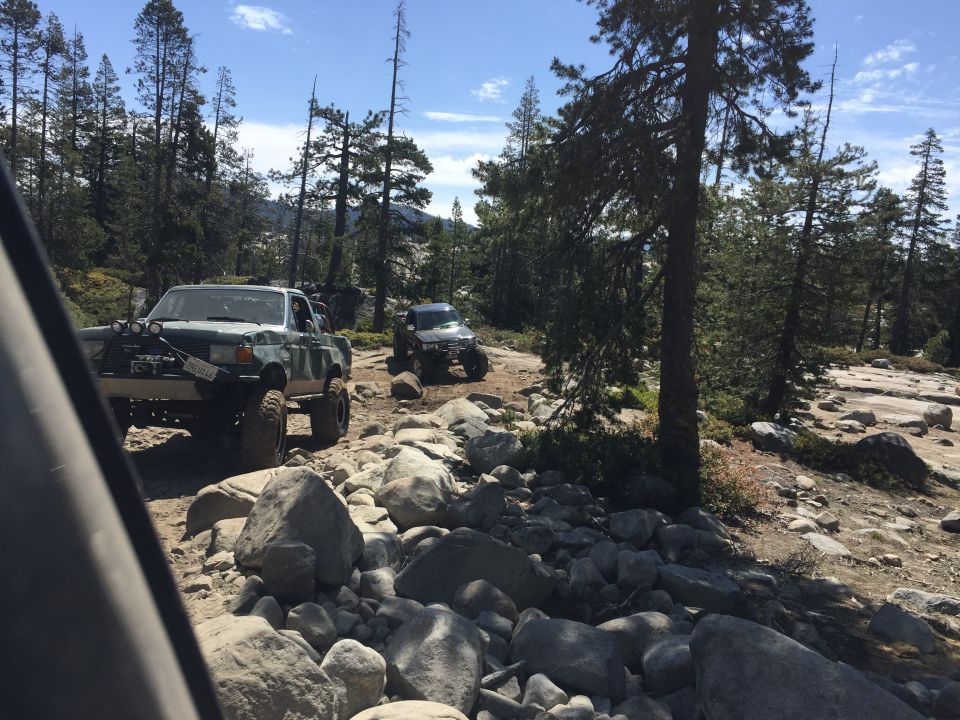 Lifted pickups on a rocky off-road trail among pine trees
