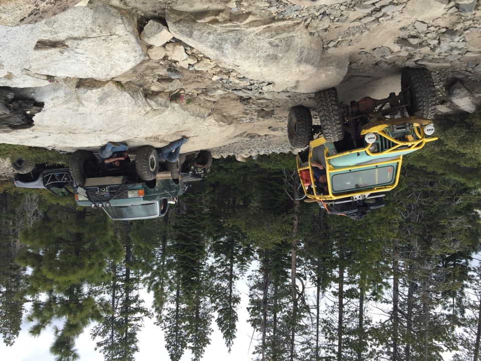 Yellow buggy and green pickup parked on rocks in a forest