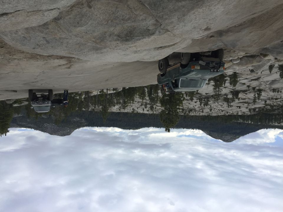 Lifted trucks parked on broad granite slopes under cloudy sky