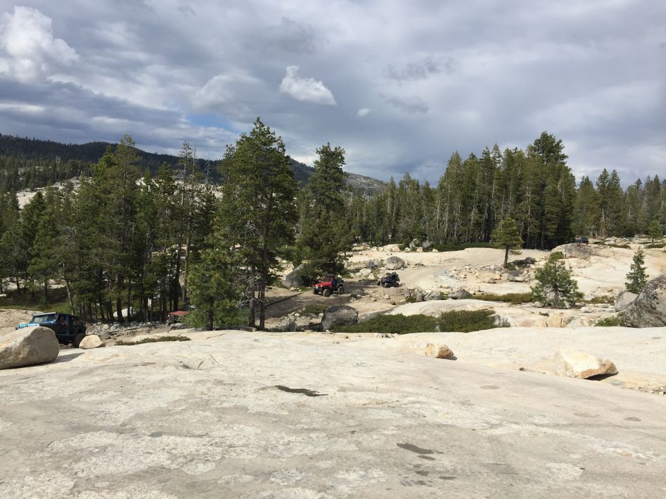 Distant off-road vehicles among trees on a granite landscape
