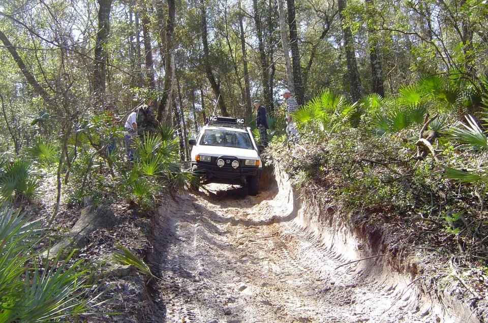White SUV with KC roof lights descending a steep rutted sand trail as spectators watch