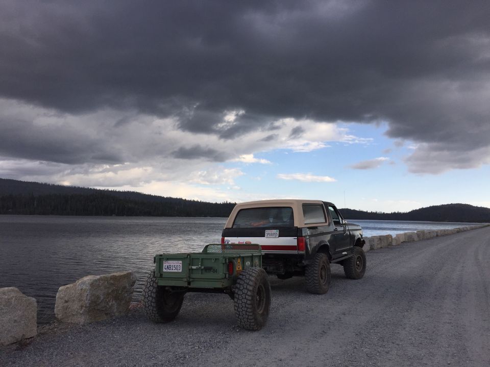 Black Ford Bronco with trailer parked on a lakeside causeway at dusk