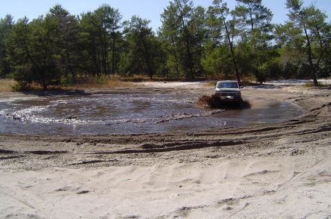 1993 Ford Bronco - A white Ford Bronco navigates a muddy obstacle course in a wooded area.
