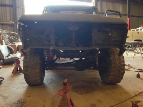 1979 Ford Bronco - The rear of a heavily modified, dark-colored Ford Bronco is shown in a workshop setting. The vehicle is lifted on jack stands, with its fro…