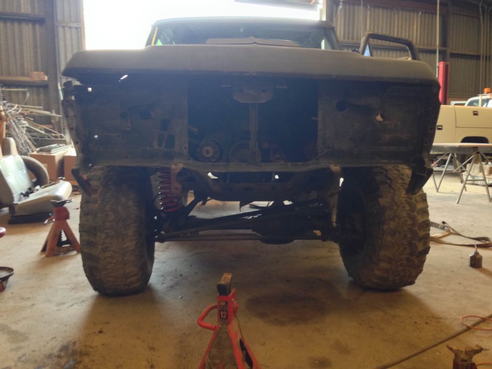 Rear view of a modified Ford Bronco, front end disassembled, on jack stands in a workshop.