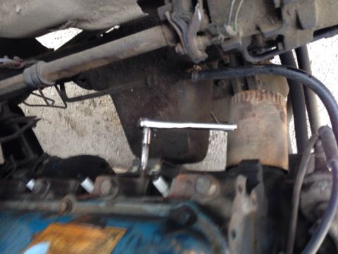 1979 Ford Bronco - A ratchet wrench is positioned over a spark plug on the blue valve cover of an engine. Various hoses and mechanical components are visible…