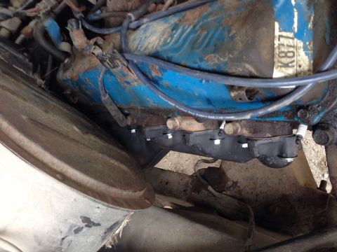 1979 Ford Bronco - A close-up view of a blue engine block with a black exhaust manifold and spark plugs visible. The engine appears to be installed in a vehic…