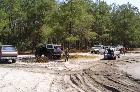 1993 Ford Bronco - A 1993 Ford Bronco is parked in a sandy area with other vehicles and people around.