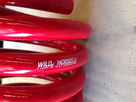 1979 Ford Bronco - A close-up shot shows a bright red coil spring, likely a suspension part for a vehicle. White text on the spring reads "WILD HORSES FOUR W…