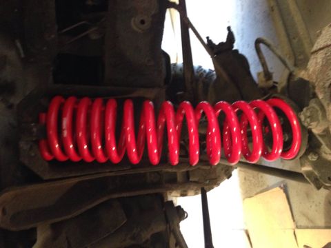 1979 Ford Bronco - A bright red, aftermarket coil spring is installed on the suspension of a vehicle. The spring is tightly wound and appears to be new.