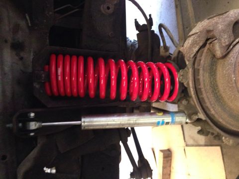 1979 Ford Bronco - A bright red coil spring and a silver Bilstein shock absorber are installed on the suspension of a vehicle, likely a Ford Bronco, with a ru…