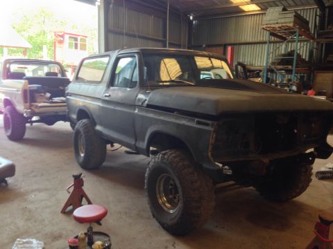 1979 Ford Bronco - A dark-colored Ford Bronco, likely a 1979 model, is parked in a garage next to a white pickup truck. The Bronco appears to be undergoing a…