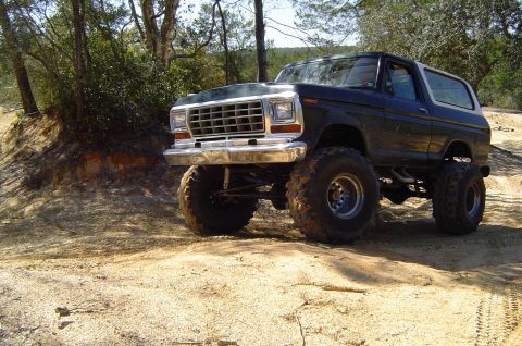 1993 Ford Bronco - This lifted dark green Ford Bronco, likely from the late 1970s, is shown off-road with prominent large tires.