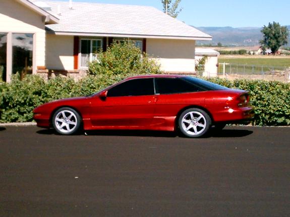 Red 1994 Ford Probe coupe with custom wheels parked in front of a house.