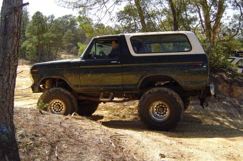 1993 Ford Bronco - This lifted Ford Bronco is navigating a challenging dirt trail, with one wheel digging into the sand.