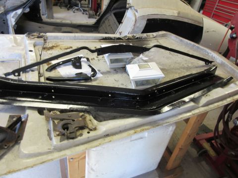 Black metal car trim pieces and hardware laid out on a workbench