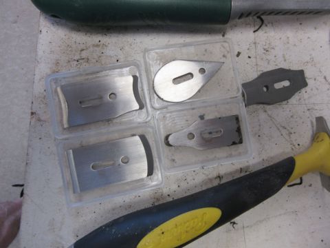 Razor blades in plastic cases and a small hammer on a dusty surface.