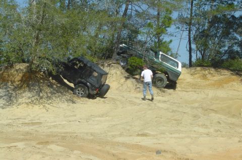 1993 Ford Bronco - Two off-road vehicles navigate a challenging sandy terrain with trees and a clear blue sky.