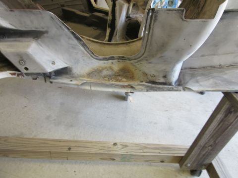 Underside of a vehicle chassis undergoing restoration, showing rust and primer.