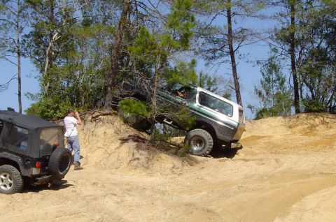 1993 Ford Bronco - A 1993 Ford Bronco navigates a steep, sandy incline off-road, with another Jeep visible in the foreground.