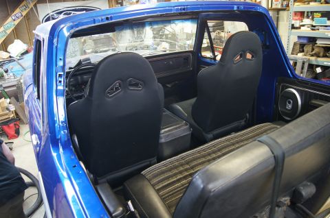 1979 Ford Bronco - The interior of a blue Ford Bronco is shown from a rear-facing angle, featuring racing seats, a center console, and a rear bench seat. The…