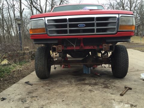 1996 Ford F-150 - Front view of a red Ford pickup truck, lifted and appearing to be under repair, with its grille and headlights clearly visible.