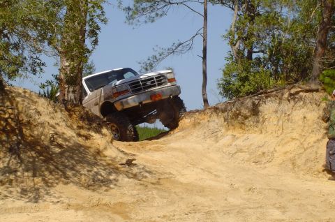 1993 Ford Bronco - A white Ford Bronco navigates a steep dirt incline with its front-left wheel lifted high.