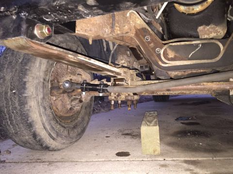 1996 Ford F-150 - Close-up of the rusty undercarriage and suspension system of a truck, with a wooden block supporting the frame.