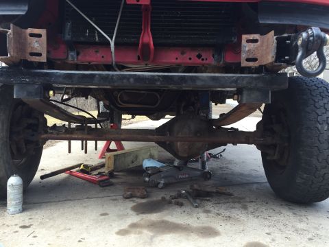 1996 Ford F-150 - The front axle and suspension components of a red 1996 Ford F-150 are visible, with tools and jacks suggesting repair work.