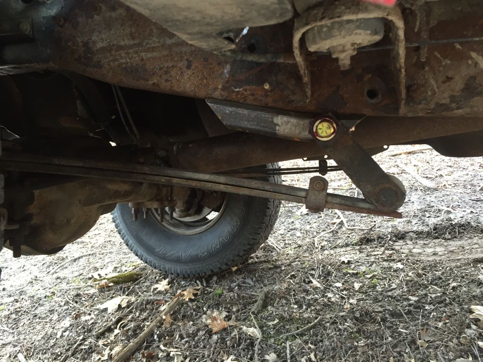 Underside view of a rusty pickup truck's rear suspension and leaf springs