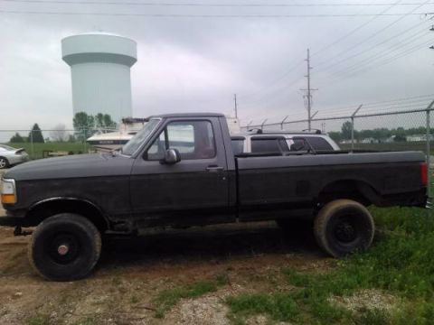1967 Ford Custom Wagon - A dark gray pickup truck is parked outdoors with a water tower and a boat visible in the background.