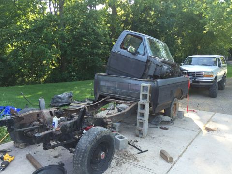 1967 Ford Custom Wagon - A truck chassis is disassembled with its cab placed in the bed, while a white SUV is parked behind it.
