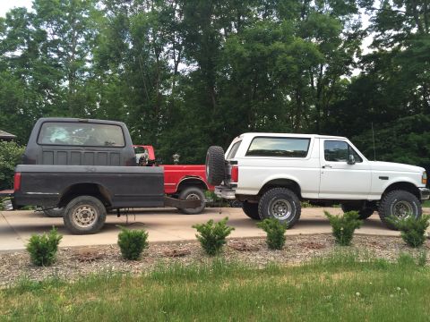 1967 Ford Custom Wagon - A black pickup truck bed is being towed by a red truck, which is in turn being towed by a white SUV.