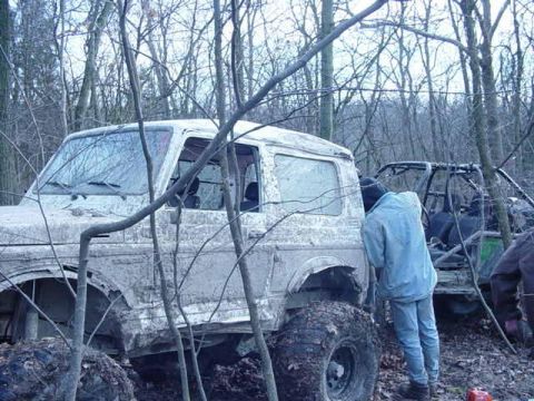 1992 Ford Bronco - Two off-road vehicles are stuck in the mud amidst a dense forest, with one person standing near the SUV.